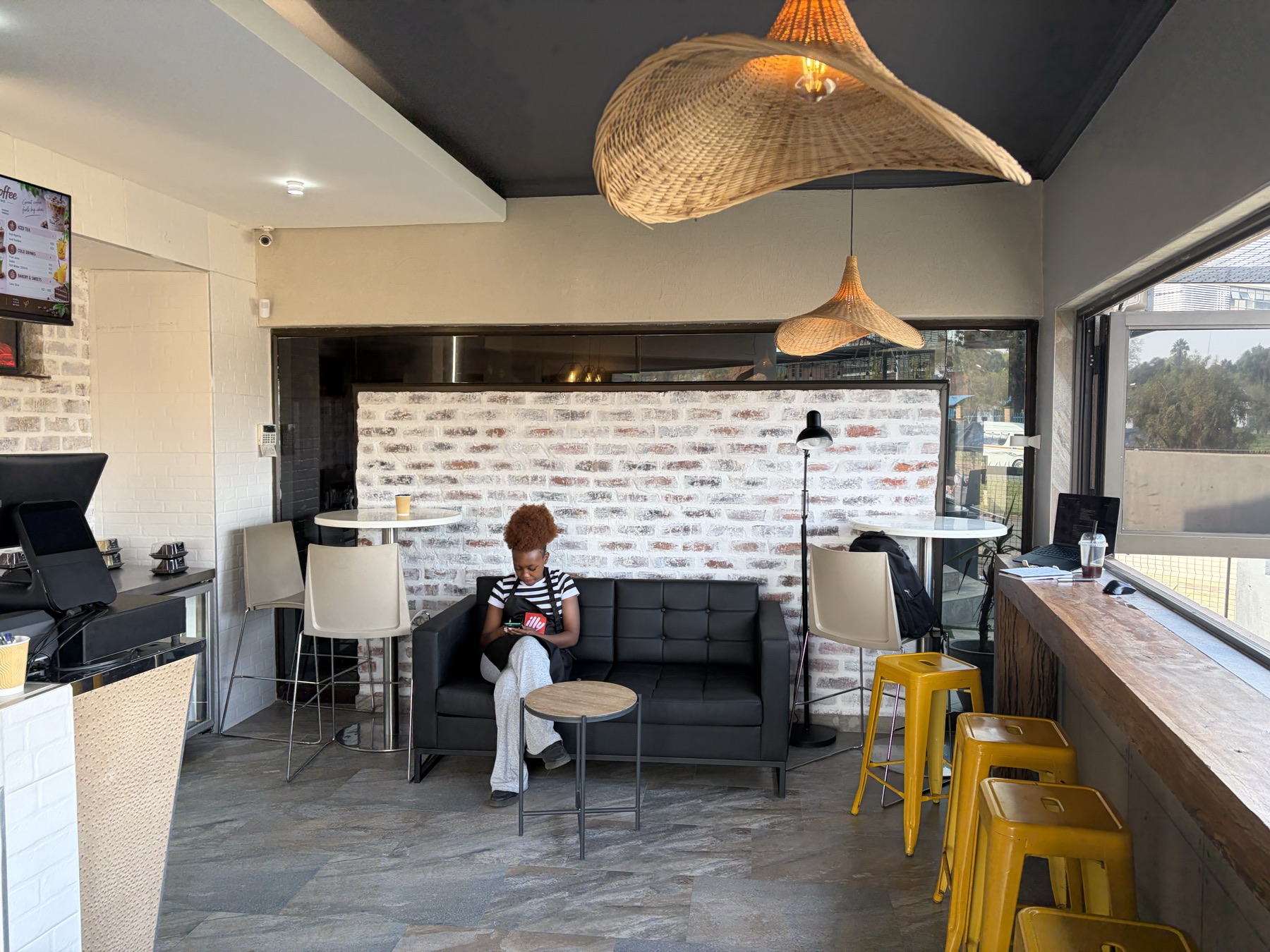 The Think-Coffee lounge: a leather couch under woven pendant lamps, high tables and yellow stools at the window bar
